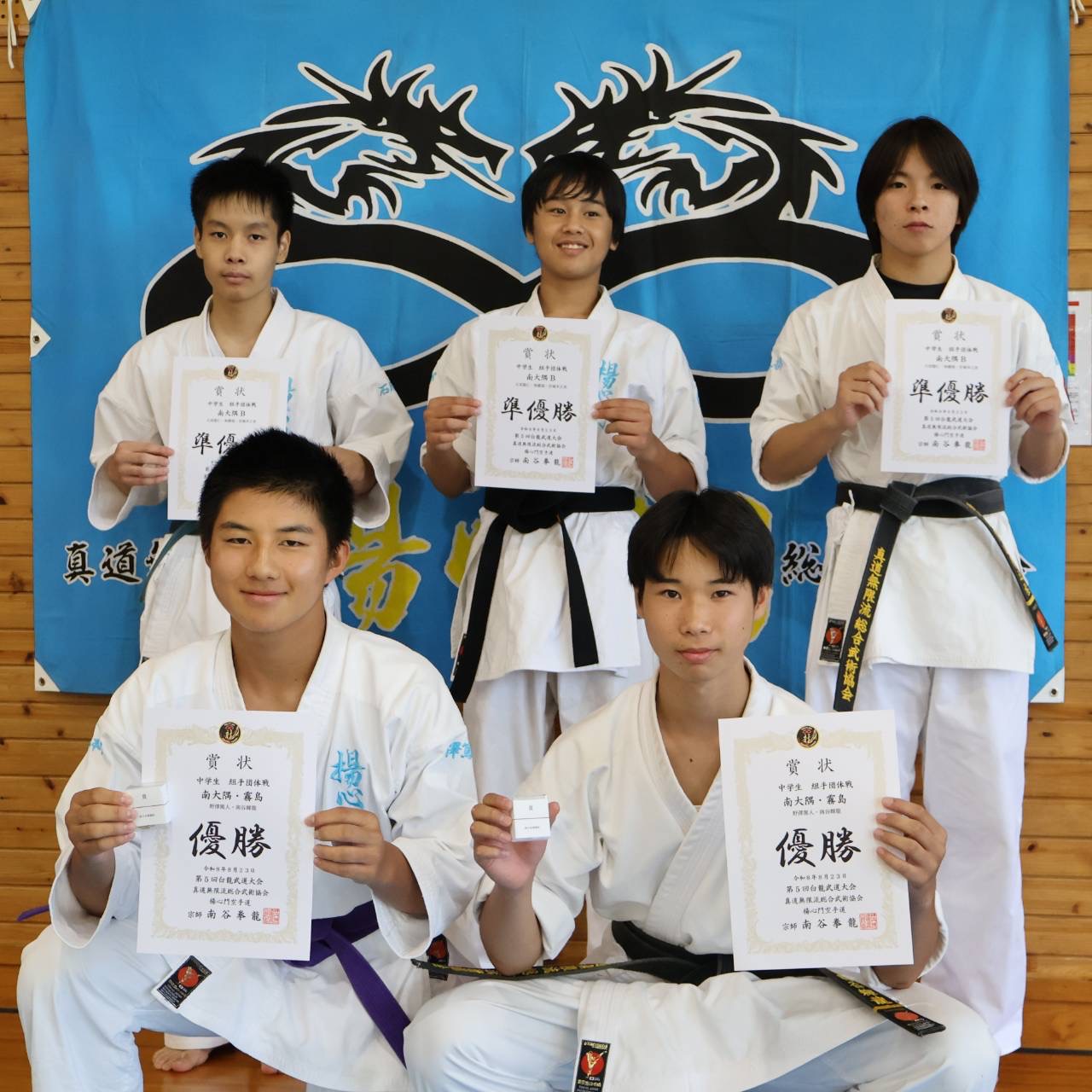 道場旗の前で優勝・準優勝の賞状を掲げる中学生の入賞者