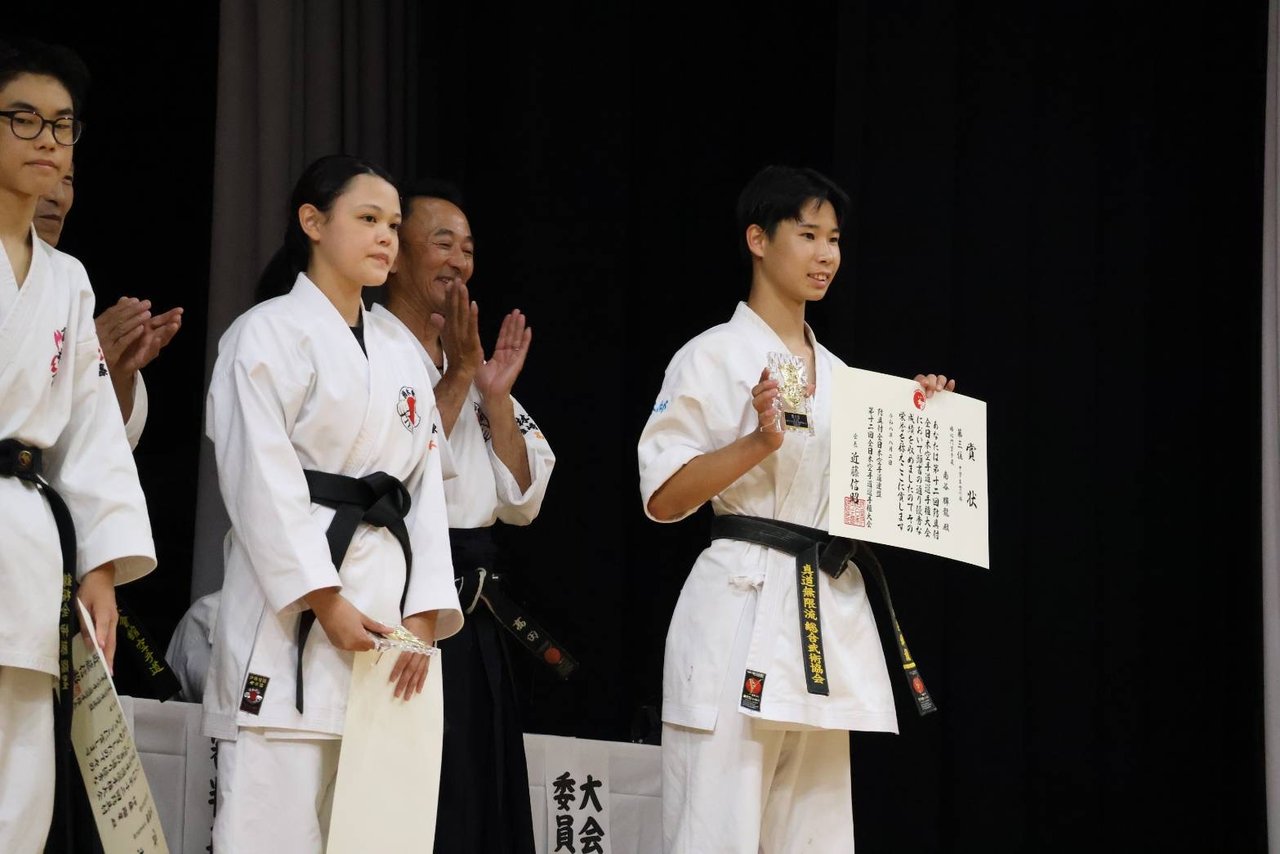 舞台上で賞状とトロフィーを受け取る門下生
