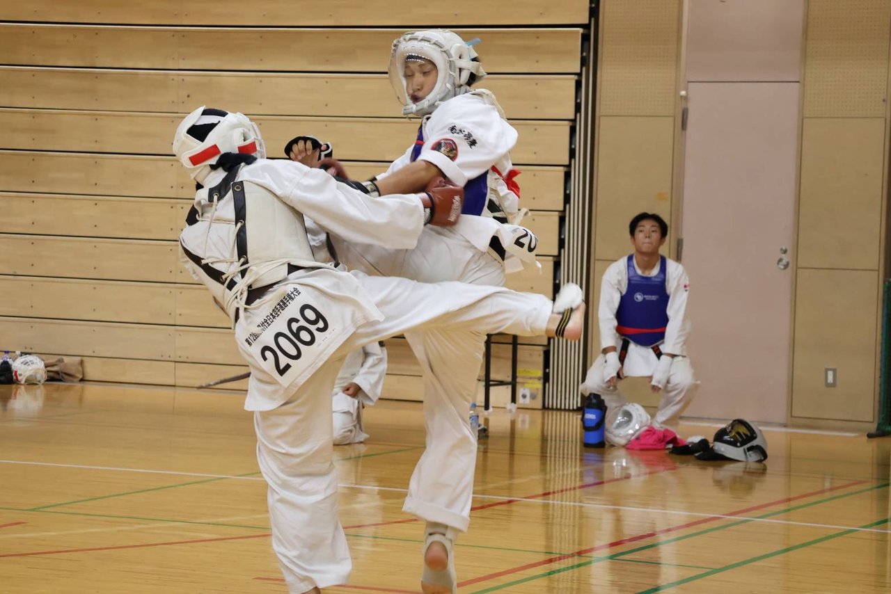 防具付組手で膝を上げ蹴りを打ち合う選手
